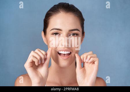 Prendendosi cura dei suoi bianchi perlacei. Studio ritratto di una giovane donna attraente che le gallina i denti su uno sfondo grigio. Foto Stock