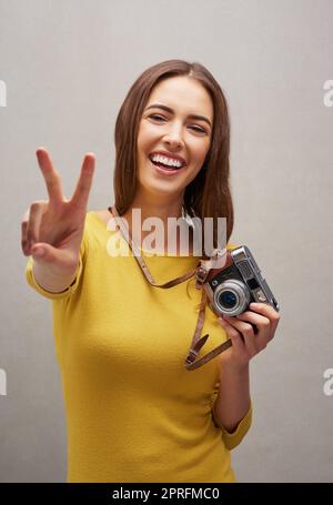 Fotografo tranquillo. Ritratto in studio di una giovane e attraente fotografa che posa con la sua fotocamera su uno sfondo grigio. Foto Stock