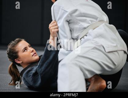 Allenamento di lottatori di arti marziali e femminili in uno studio di allenamento con un avversario. Donna in forma, giovane e attiva in una lezione di difesa a un dojo. Atleta che pratica jujutsu con un partner. Foto Stock