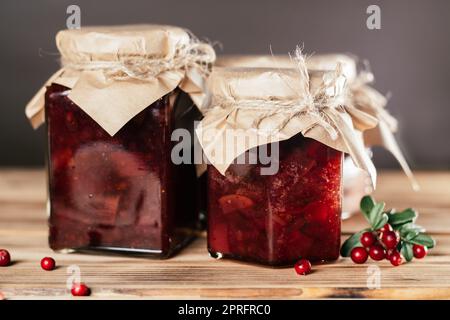 Vasetti di marmellata di lingoni e pere fatta in casa con carta artigianale su coperchi su superficie di legno accanto a lingoni freschi Foto Stock