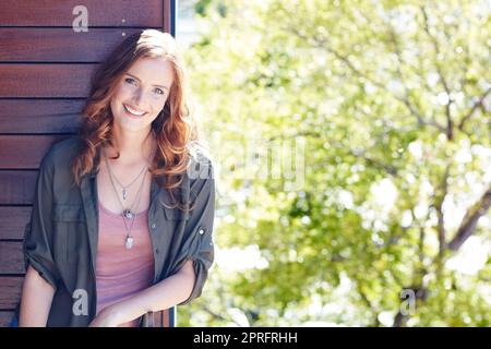 Radiosamente felice. Ritratto di una giovane donna attraente che si posa contro una parete di legno. Foto Stock