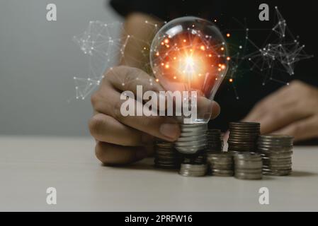 Innovazione creatività crescita idea successo economia strategia di sviluppo business concept.Hand holding lampadina sulla pila di monete risparmio denaro sulla scrivania. Foto Stock