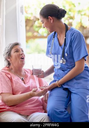 Questo vi farà sentire di nuovo meglio in un istante: Un'infermiera che dà un farmaco e un bicchiere d'acqua a un paziente anziano. Foto Stock