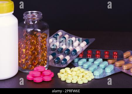 Le pillole e le compresse di diversi colori sono sparse e in bottiglie su uno sfondo scuro Foto Stock