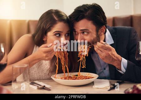 Una corsa al traguardo: Una giovane coppia che condivide un piatto di spaghetti durante una cena romantica in un ristorante. Foto Stock