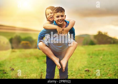 Fanno una coppia adorabile. Ritratto di un adorabile ragazzino che dà alla sorellina un giro in piggyback all'esterno. Foto Stock