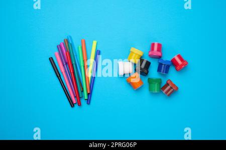 Pennarelli multicolore e vernice acrilica in vaso di plastica su sfondo blu, vista dall'alto Foto Stock