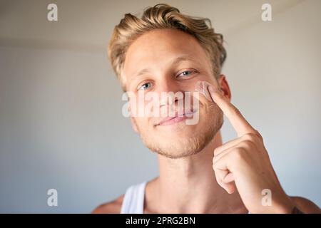 Usando moisturizer farà un mondo di differenza. Un giovane uomo che applica moisturizer al suo viso. Foto Stock