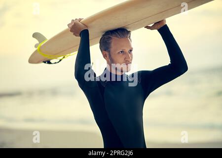 I surfisti hanno l'acqua salata nelle loro vene, un giovane surfista rilassato che guarda le onde mentre tiene la tavola da surf in spiaggia. Foto Stock