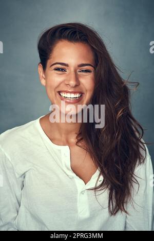 Youre mai completamente vestito senza un sorriso. Ritratto di una bella giovane donna sorridente su uno sfondo grigio in studio. Foto Stock