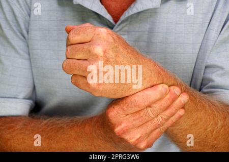 Dita della mano destra di un uomo maturo bianco che massaggia il polso sinistro Foto Stock