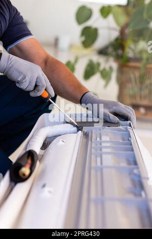 Mani di un tecnico maschio che utilizza un cacciavite per fissare il moderno condizionatore d'aria in ambienti interni. Foto Stock