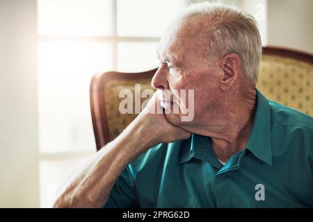 Il tempo si ferma quando youre vecchio. Un uomo anziano che guarda premuroso mentre si siede da solo in un salotto. Foto Stock