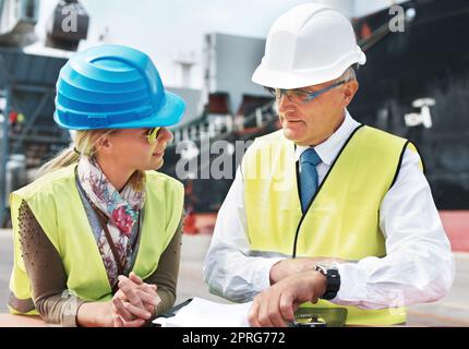 Lavoratori portuali, lavoratori del settore delle spedizioni e delle spedizioni di merci in attrezzature di sicurezza che lavorano su documenti logistici del trasporto. Supply chain, amministrazione e manager in collaborazione e conversazione Foto Stock