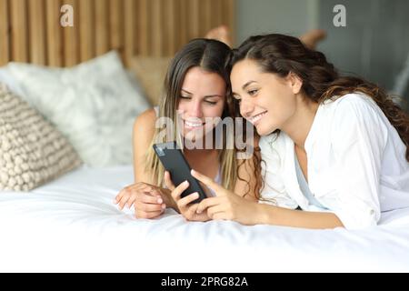 Due amici che controllano lo smartphone sdraiati su un letto Foto Stock