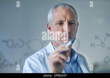 Figurando i suoi risultati. Uno scienziato maschio che disegna strutture molecolari su una parete di vetro in un laboratorio. Foto Stock