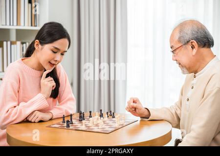 Bella giovane donna sorridere che si diverte seduto a giocare a scacchi con anziani a casa Foto Stock