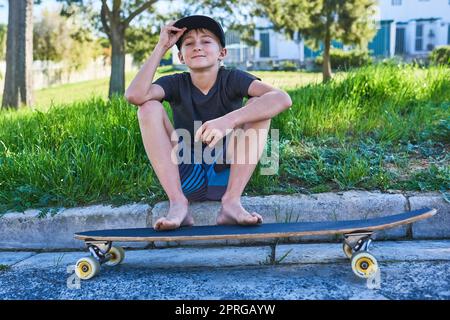 Io e il mio longboard. Ritratto completo di un ragazzo seduto sul marciapiede con il suo longboard. Foto Stock