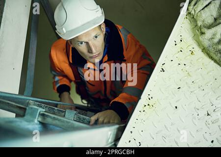 Gli ingegneri hanno paura delle altezze. Foto di un giovane ingegnere in equipaggiamento di sicurezza che sale su una scala. Foto Stock