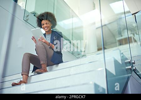 Lavorando online con alcune idee innovative, una giovane donna d'affari che utilizza un tablet digitale sulle scale di un ufficio moderno. Foto Stock