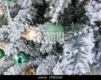 Palline verdi lucenti sull'albero di Natale. Perle bianche sui rami di abete rosso. I rami sono ricoperti di ghiaccio. Sfondo natalizio o capodanno Foto Stock