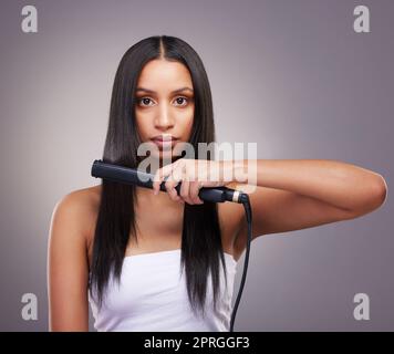 Un calore eccessivo può danneggiare i capelli. una giovane donna attraente in piedi da sola in studio e utilizzando una piastra per capelli per lo stile dei suoi capelli Foto Stock
