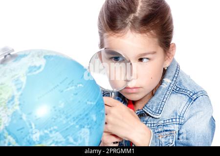 Curiosa bambina che guarda attraverso lente d'ingrandimento sul globo Foto Stock