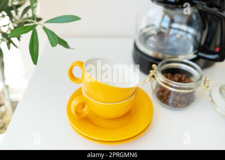 Bella mattina, il processo di preparazione del caffè. Una macchina per caffè antigoccia automatica è dotata di una tazza gialla su un tavolo bianco. Cucina elettrica piccolo hous Foto Stock