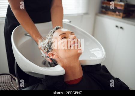 Capelli, sorriso e lavaggio, donna in salone relax con testa indietro e pulizia parrucchiere con shampoo e balsamo. Bellezza, cura dei capelli e un massaggio di lusso Foto Stock