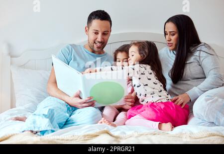 Voglio sapere cosa succederà dopo. un uomo che tiene un libro di storia mentre siede con la sua moglie e due figlie Foto Stock