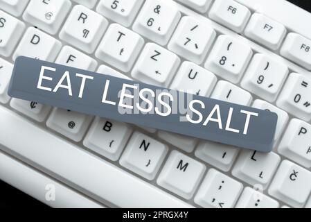 Insegna scritta a mano Eat Less Salt. Parola per ridurre la quantità di sodio nella vostra dieta mangiare sano messaggi importanti presentati su pezzo di carta sulla scrivania con libri. Foto Stock