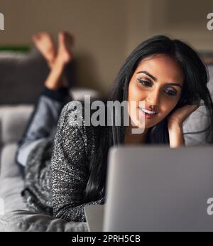 Recuperare i feed dei social media. Una giovane donna che naviga in rete sdraiata sul divano di casa. Foto Stock