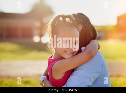 Mommys sempre lì con un abbraccio. Ritratto di una bambina sorridente che abbraccia la madre mentre si gode una giornata insieme nel parco. Foto Stock