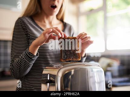 L'ho lasciato troppo a lungo. Una donna che rimuove una fetta di pane tostato bruciato da un tostapane a casa. Foto Stock