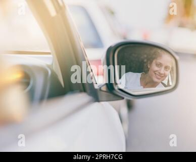 La vigilanza la mantiene al sicuro sulla strada. Una giovane donna che guarda nello specchio laterale della sua auto durante la guida. Foto Stock