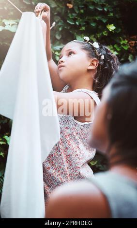 Insegnare la responsabilità dei bambini coinvolgendoli nei chores. Una madre e la sua figlia piccola appendere su lavanderia su una linea di lavaggio all'aperto. Foto Stock