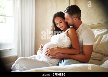 Non possono aspettare di tenere in mano il loro bambino: Un marito e una moglie incinta seduti insieme in una camera da letto. Foto Stock