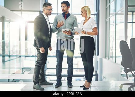 Discutere nuove strategie. Un gruppo di colleghi che parlano insieme su un tablet digitale in un ufficio. Foto Stock