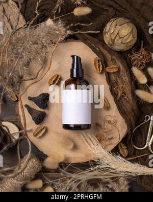 Una bottiglia cosmetica con pompa su legno vicino alle decorazioni boho naturali vista dall'alto. Etichetta Mockup Foto Stock