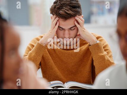 Studio, stress e studente all'università con ansia per un test. Giovane uomo con mal di testa, preoccupato e studiando con il libro di testo sulla scrivania in biblioteca. Stanco Foto Stock