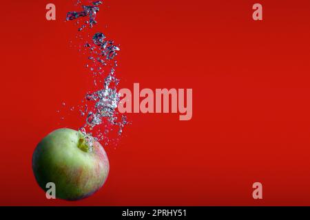 mela su sfondo rosso che spruzza in acqua bolle fresche spruzzano frutta Foto Stock