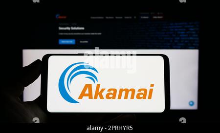 Persona che detiene uno smartphone con il logo della società statunitense Akamai Technologies Inc. Sullo schermo di fronte al sito Web. Messa a fuoco sul display del telefono. Foto Stock