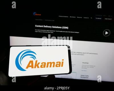 Persona che tiene il cellulare con il logo della società statunitense Akamai Technologies Inc. Sullo schermo di fronte alla pagina Web aziendale. Messa a fuoco sul display del telefono. Foto Stock