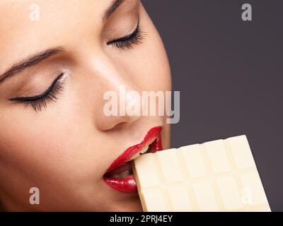 Altrettanto buono quanto il genere scuro. Primo piano ritratto di una giovane femmina carina mordente in un pezzo di cioccolato Foto Stock