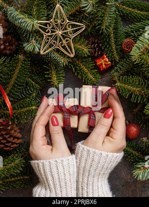 Mani femminili che tengono due confezioni regalo su un tavolo di legno vicino alle decorazioni natalizie, vista dall'alto Foto Stock