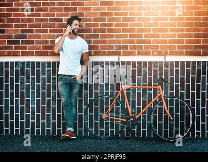 Tutti componono il suo numero, un bel giovane in piedi accanto alla sua bicicletta e usando un telefono in città. Foto Stock