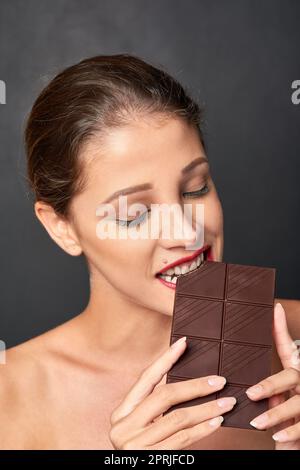 Ceneri un amante del cioccolato. Studio girato di una giovane donna attraente che è tentato da qualcosa di dolce. Foto Stock