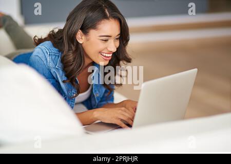 Scopri le foto delle sue vacanze con gli amici. Una giovane donna attraente che usa il suo notebook mentre si sdraia sul divano. Foto Stock