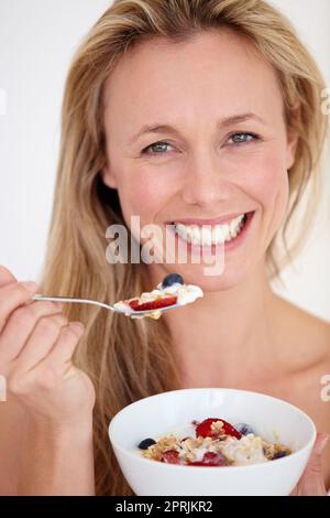 Mangiare sano mantiene la sua giovane. Bella donna sorridente felice mentre si gode una sana ciotola di colazione Foto Stock