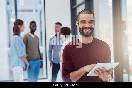 Posso fare tutto in movimento. Ritratto corto di un giovane uomo d'affari che lavora in ufficio con i suoi colleghi sullo sfondo. Foto Stock